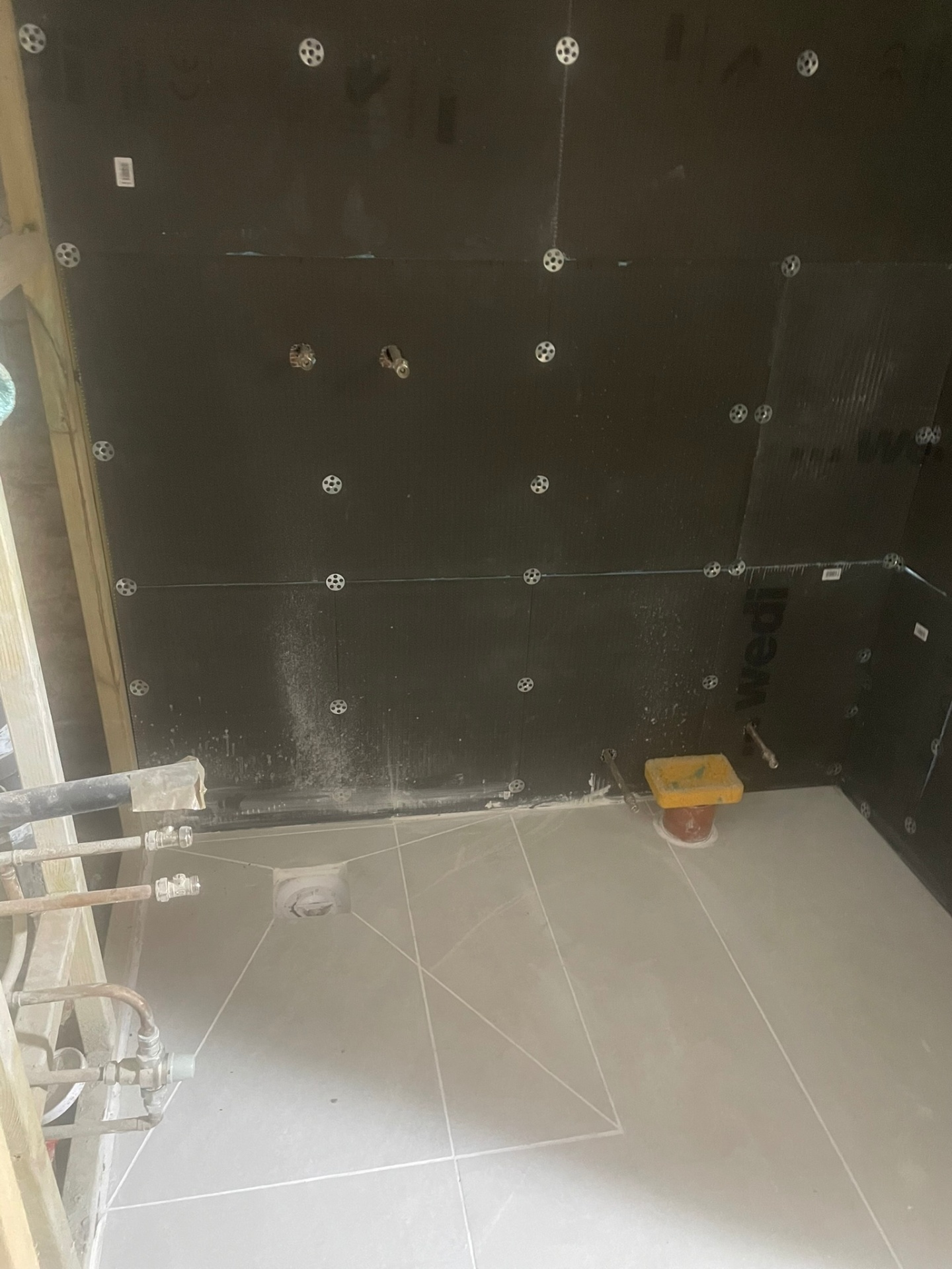 Wet room at the tanking stage — black waterproof boards with circular fixings and a grey sloped floor base — Ash Villa waterproofing