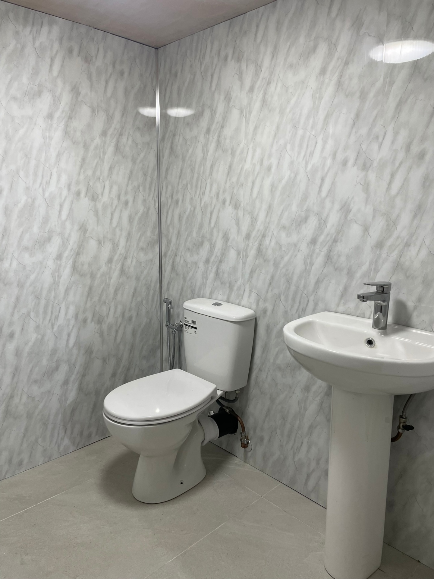 Simple cloakroom with grey marble wall panels, white toilet and pedestal basin installed by Ash Villa