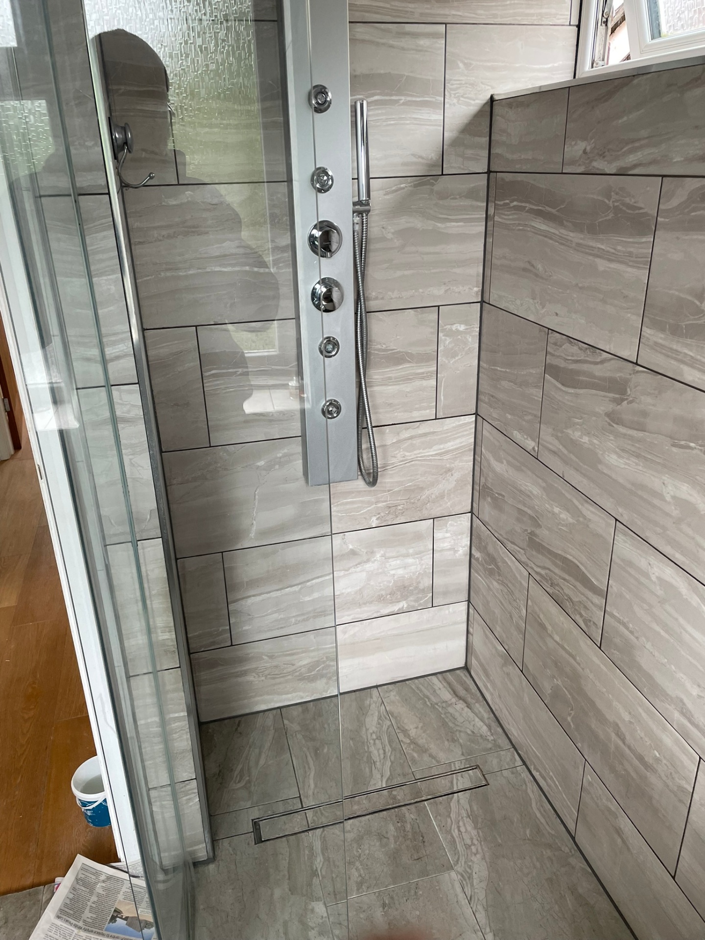 Fully tiled wet room with marble-effect walls, chrome shower panel and linear drain, installed by Ash Villa in Ealing