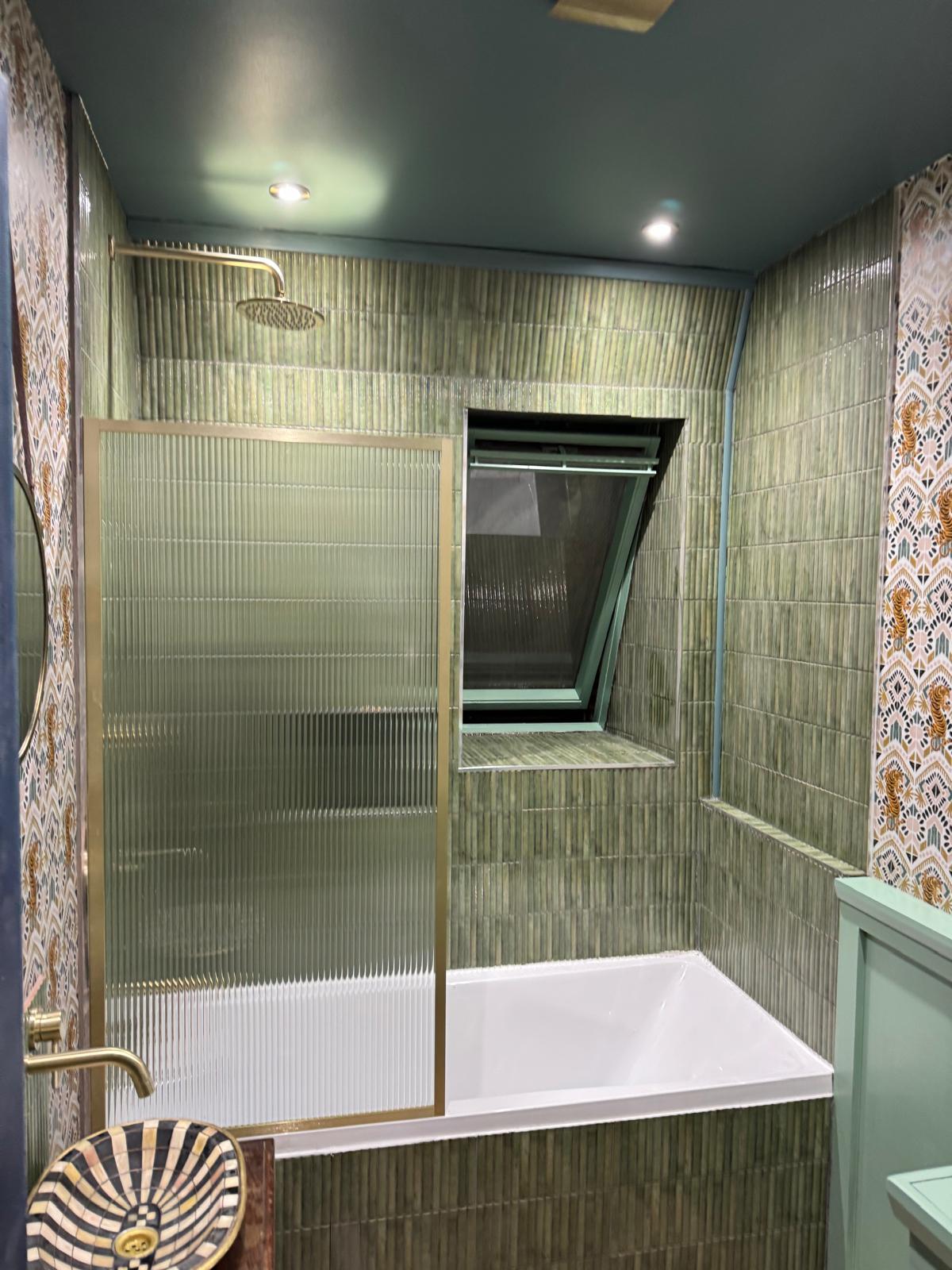 Bath and shower combination with brushed brass reeded glass screen and green tiled walls, bathroom installation in West London
